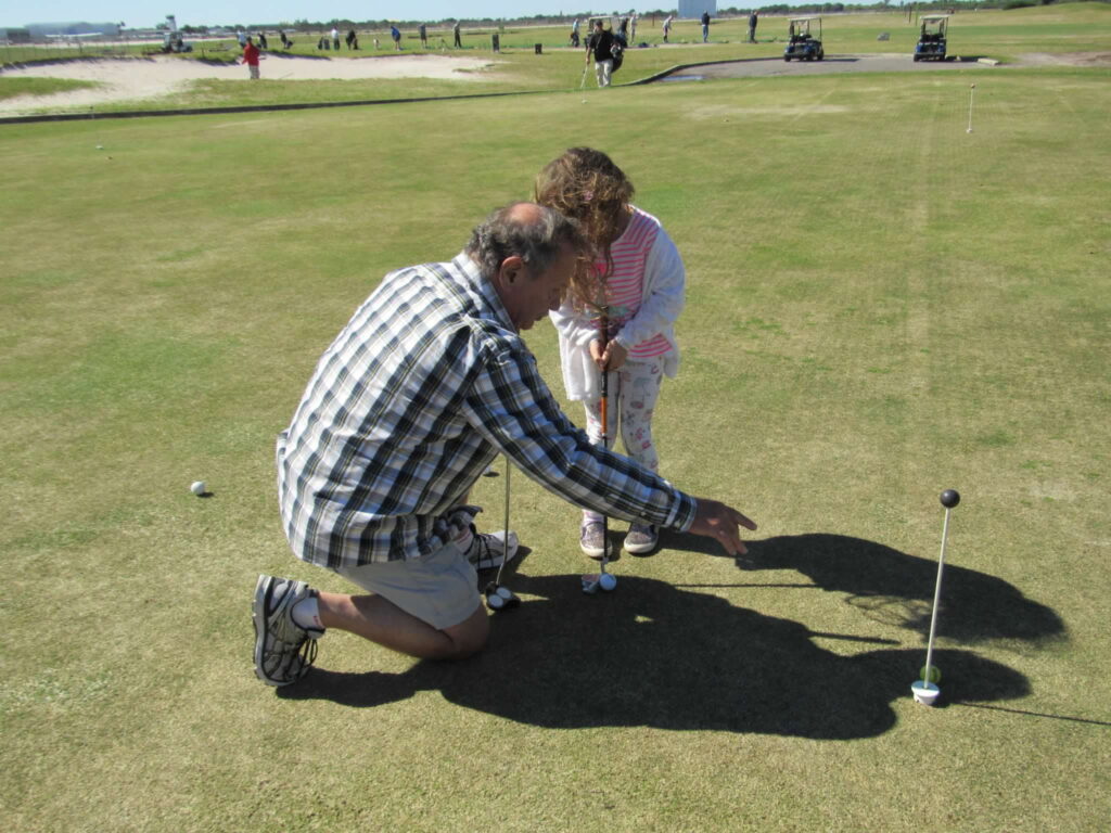 A family photo of Caprina putting on the golf green with her grandpa helping.